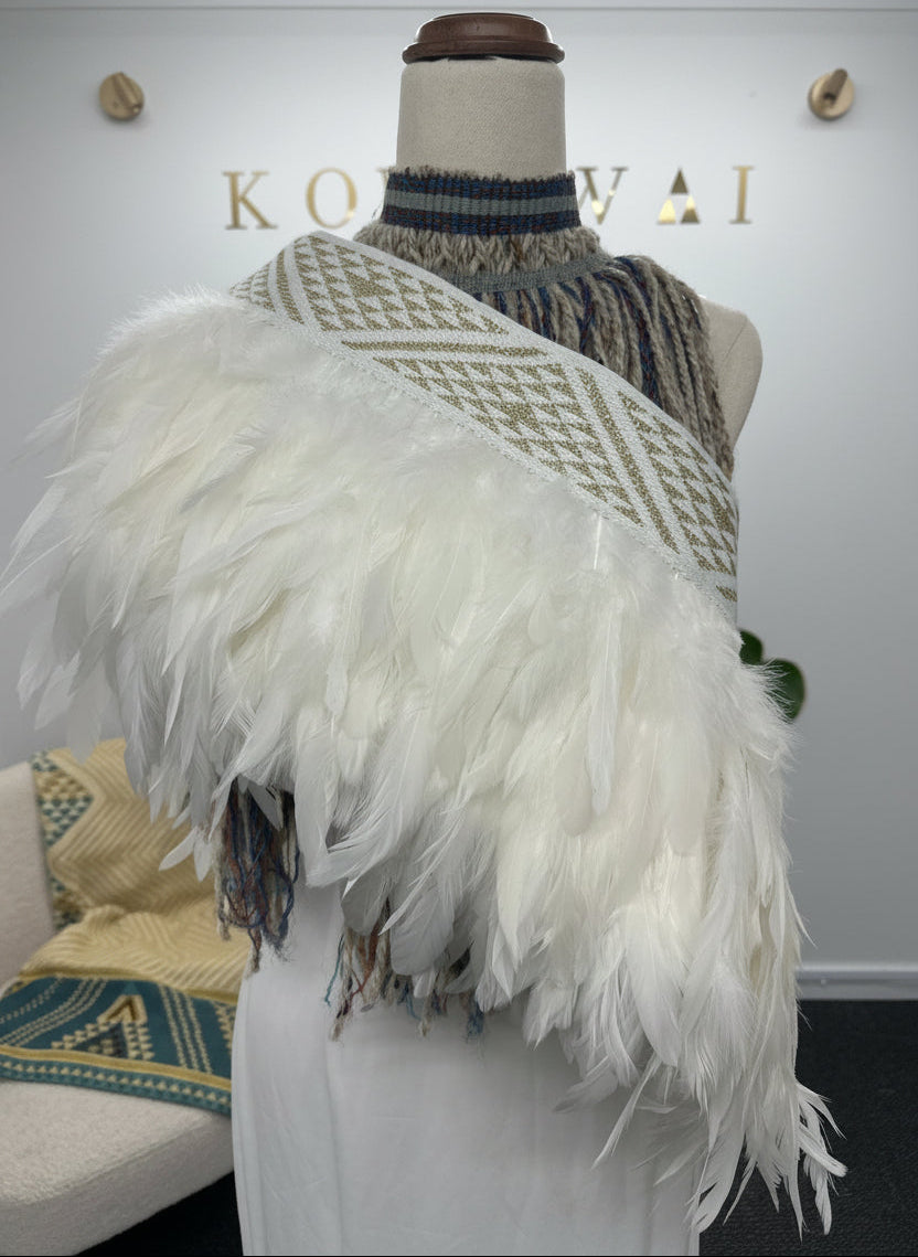 A white feathered shawl with a geometric patterned knit collar and fringe, displayed on a mannequin torso in a boutique setting.