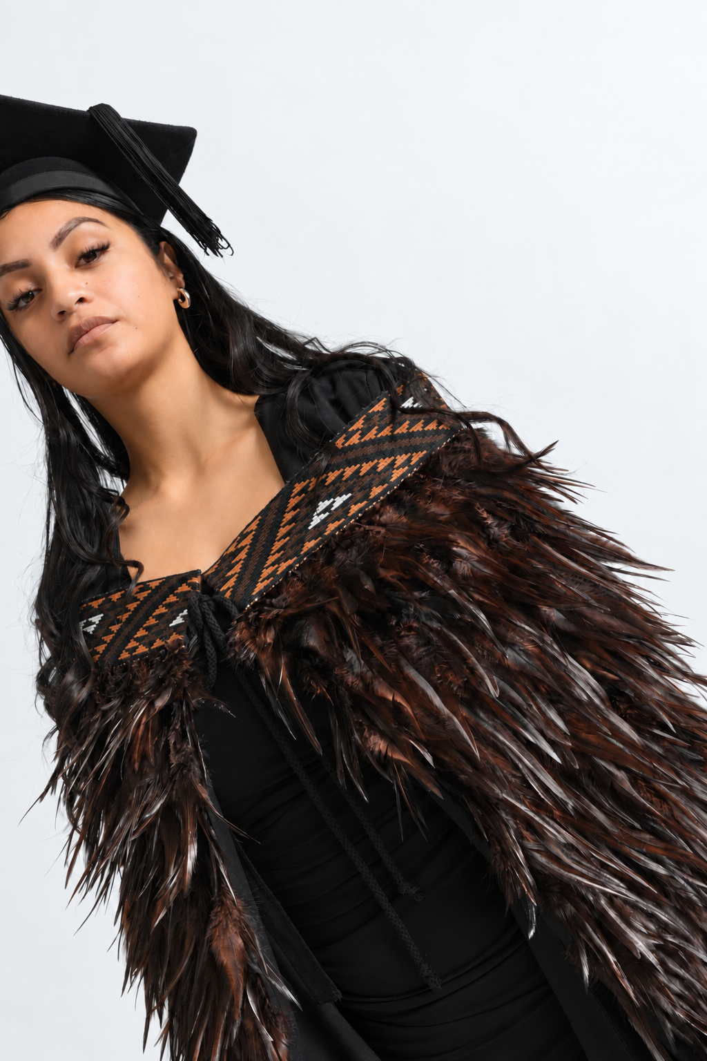 Angled close-up of the Kahu Kiwi tāniko band and chocolate feathers worn by a graduate.