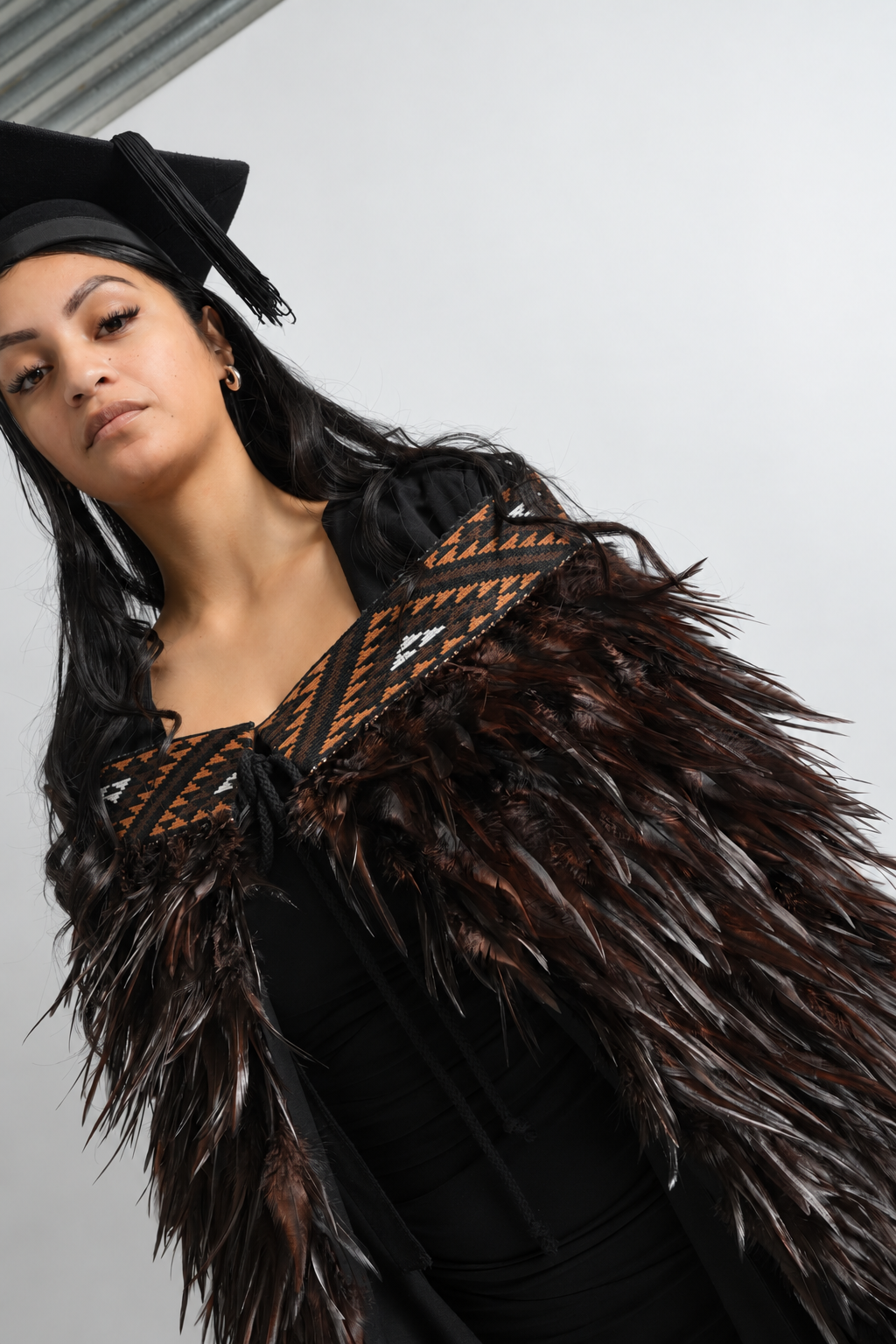 Angled close-up of the Kahu Kiwi tāniko band and chocolate feathers worn by a graduate.