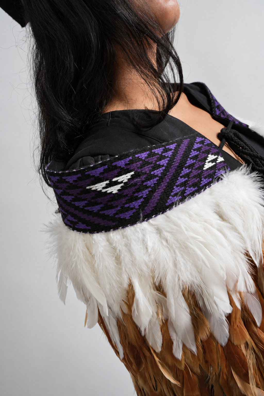 Close-up of Wairua Purple tāniko and white feathers worn by a graduation model