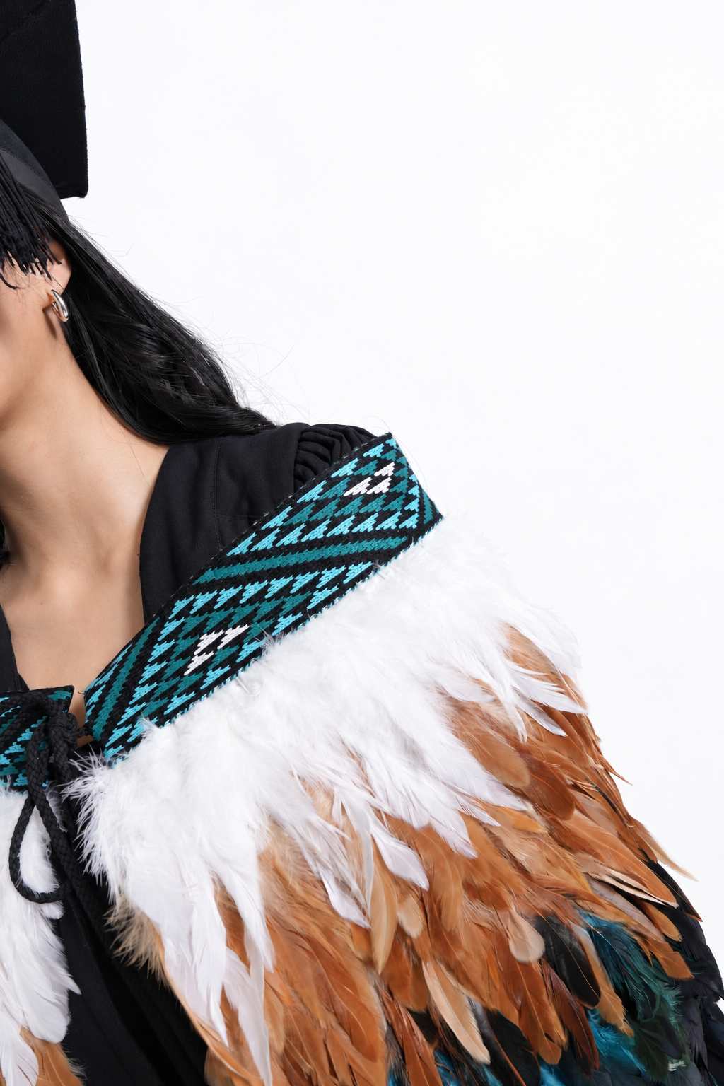 Close-up of Kingfisher Blue tāniko and white, warm brown and teal feathers worn by a graduation model.