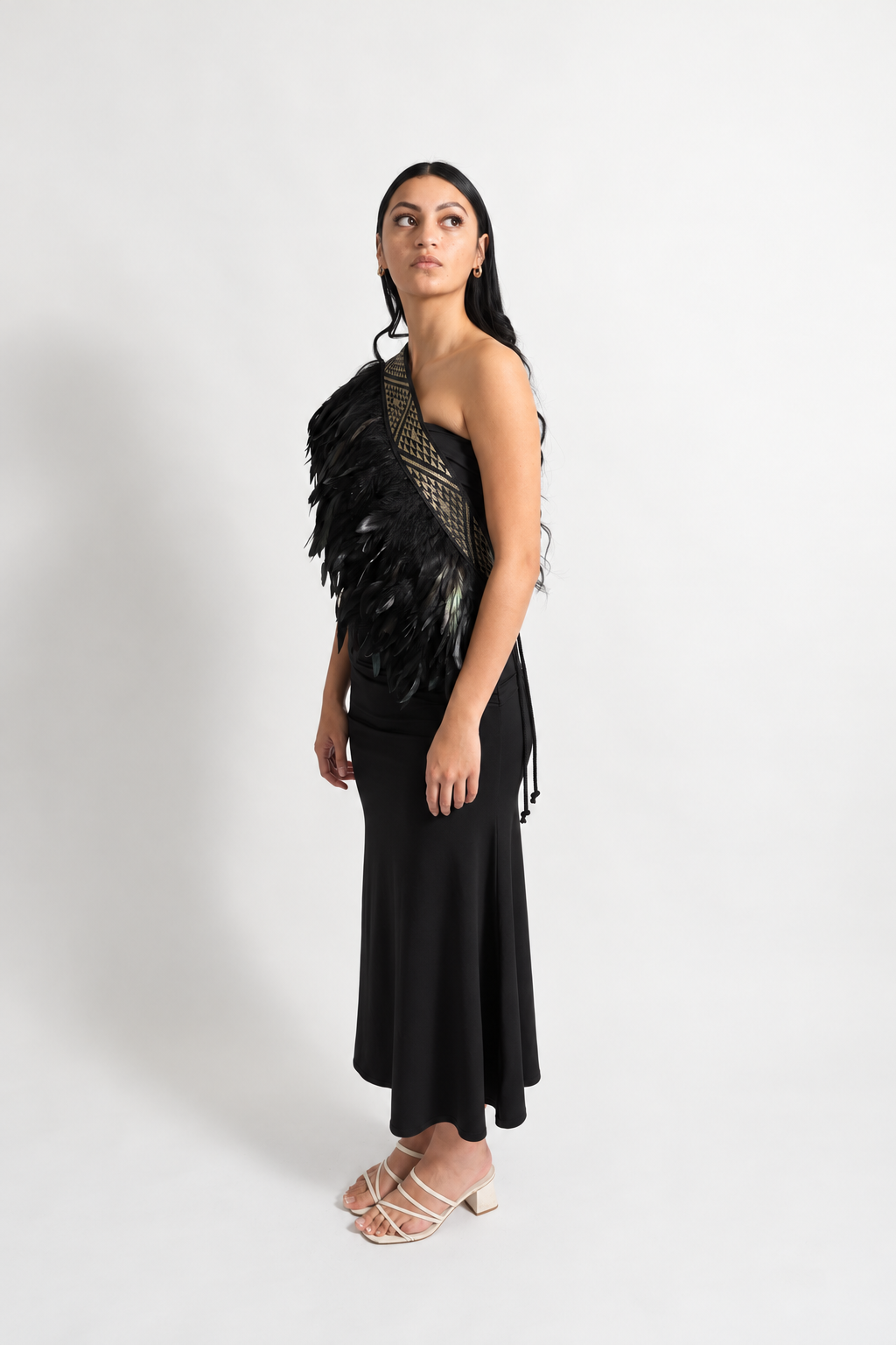 Female model wearing black Pīataata korowai with a gold tāniko band in a side pose.