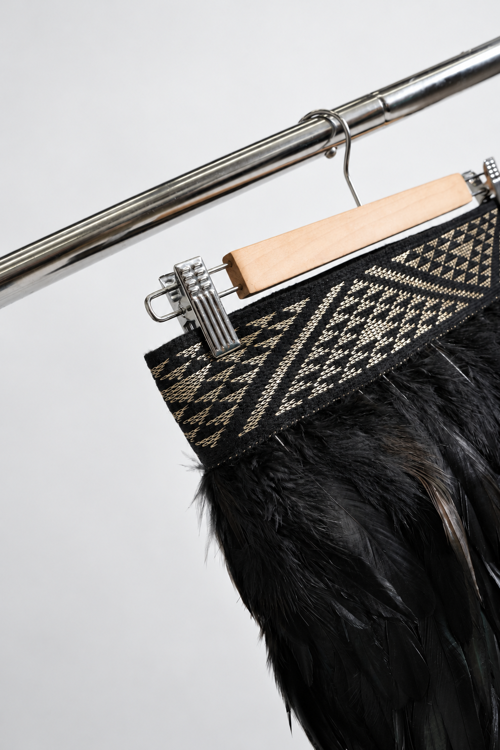 Gold and black Pīataata tāniko band close-up on a wooden hanger and clothing rack.