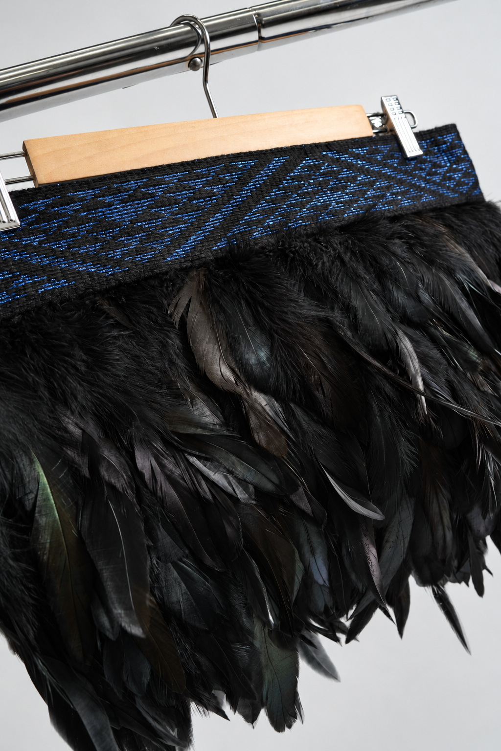 Pāua blue and black Pīataata tāniko band close-up on a wooden hanger and clothing rack.