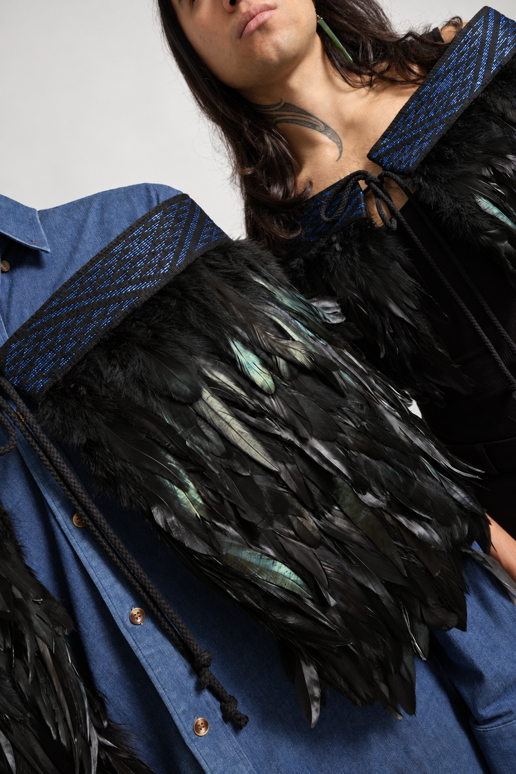 Close-up of pāua blue tāniko bands and the texture of black Pīataata feathers while worn.