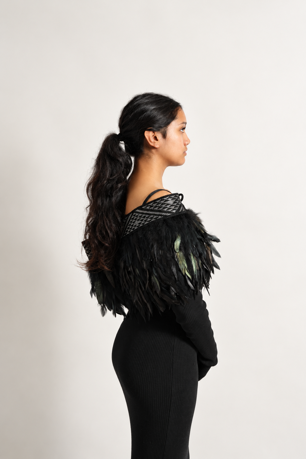 Female model wearing black Pīataata korowai with a silver tāniko band, viewed from the side.