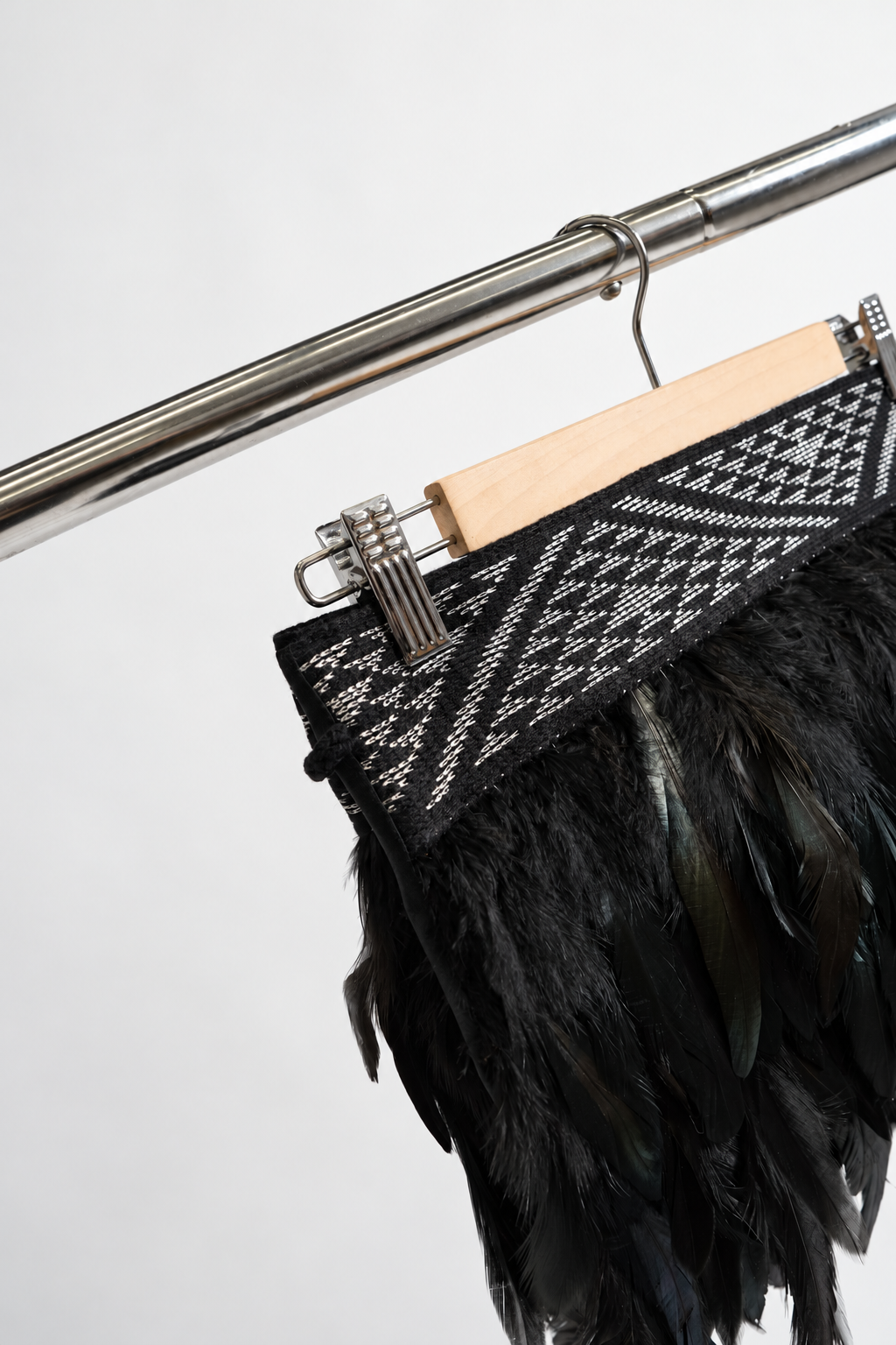 Silver and black Pīataata tāniko band close-up on a wooden hanger and clothing rack.