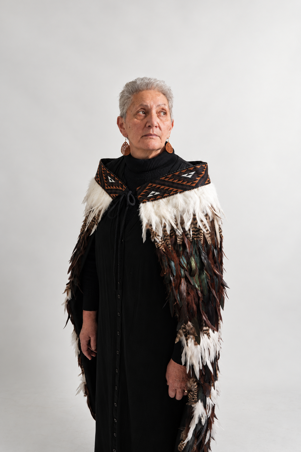 Angled portrait of a woman wearing the chocolate Tuku Iho korowai with three white feather lines and brown KBH tāniko band.