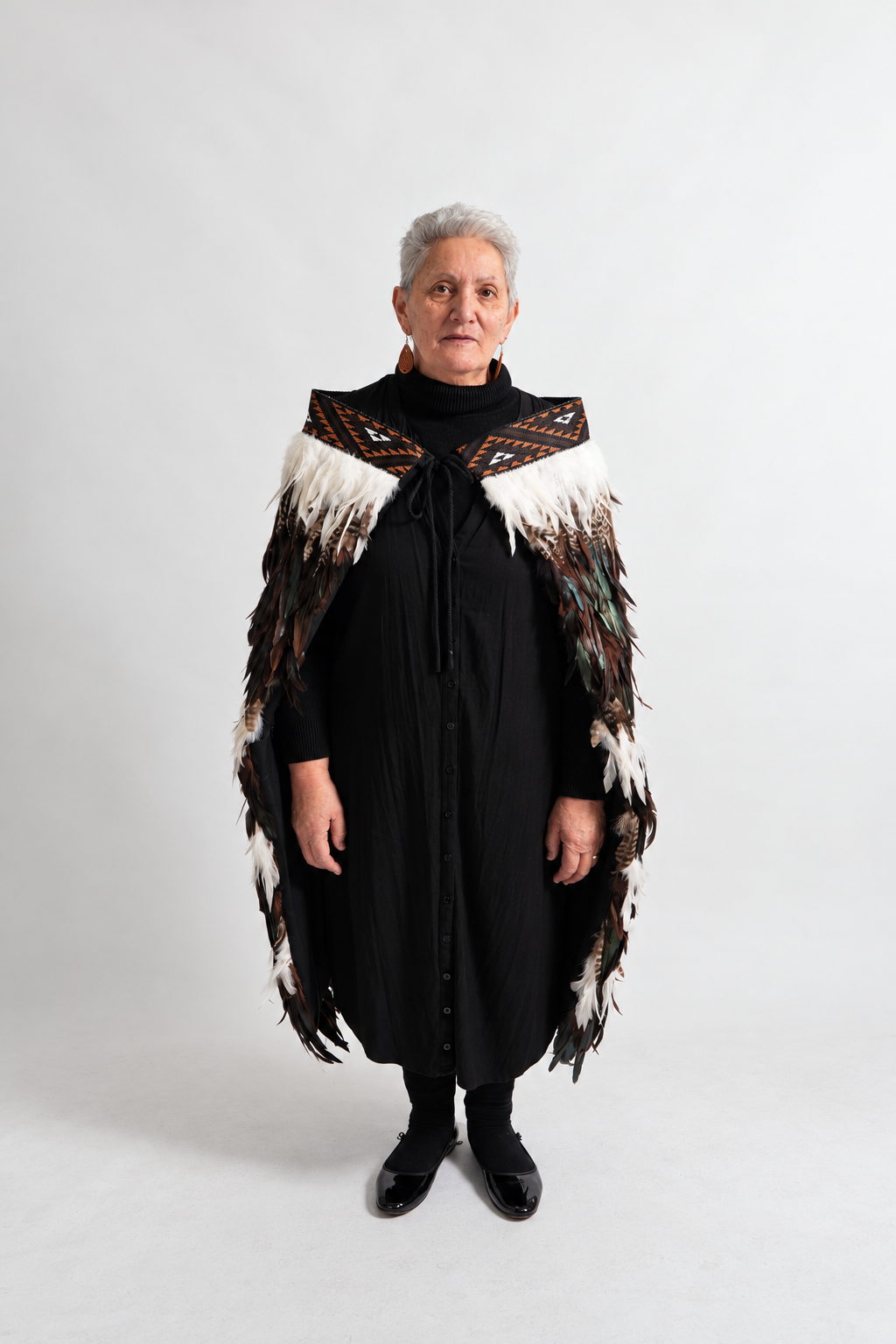 Woman wearing the full-length chocolate Tuku Iho korowai, showing its three white feather lines.