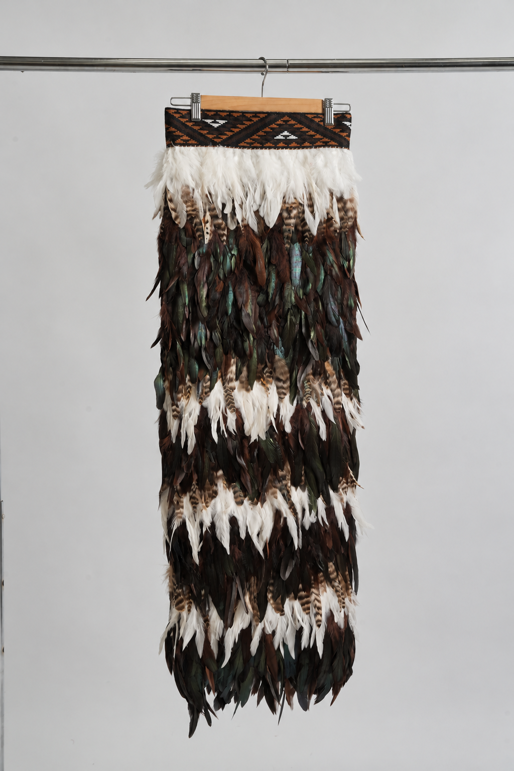 Full-length Tuku Iho chocolate brown korowai with three white feather lines representing three generations and a brown KBH tāniko band.